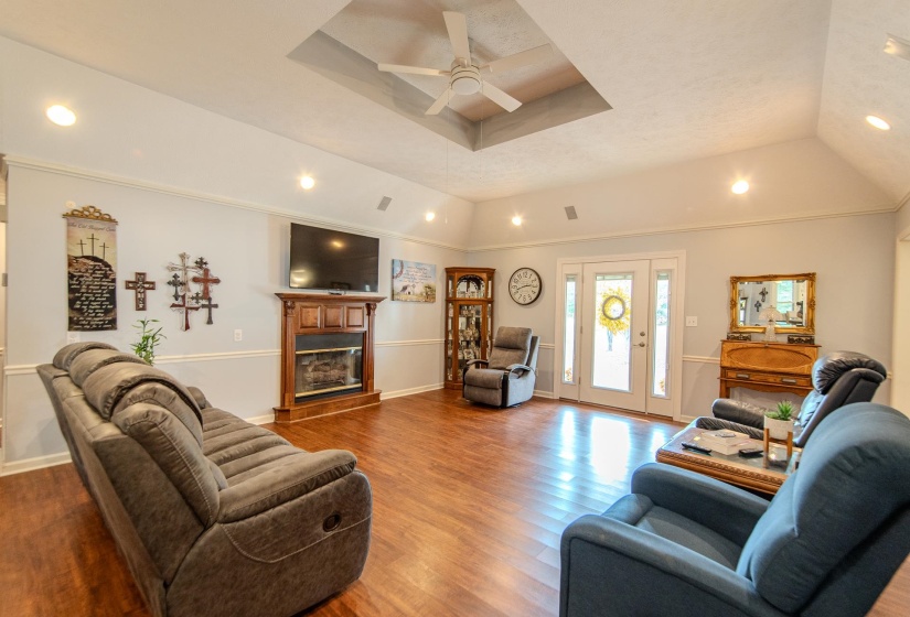 Living room featuring a raised ceiling, recessed lighting, wood finished floors, a glass covered fireplace, and ceiling fan