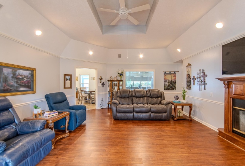 Living room featuring a tray ceiling, recessed lighting, wood finished floors, a ceiling fan, and a glass covered fireplace