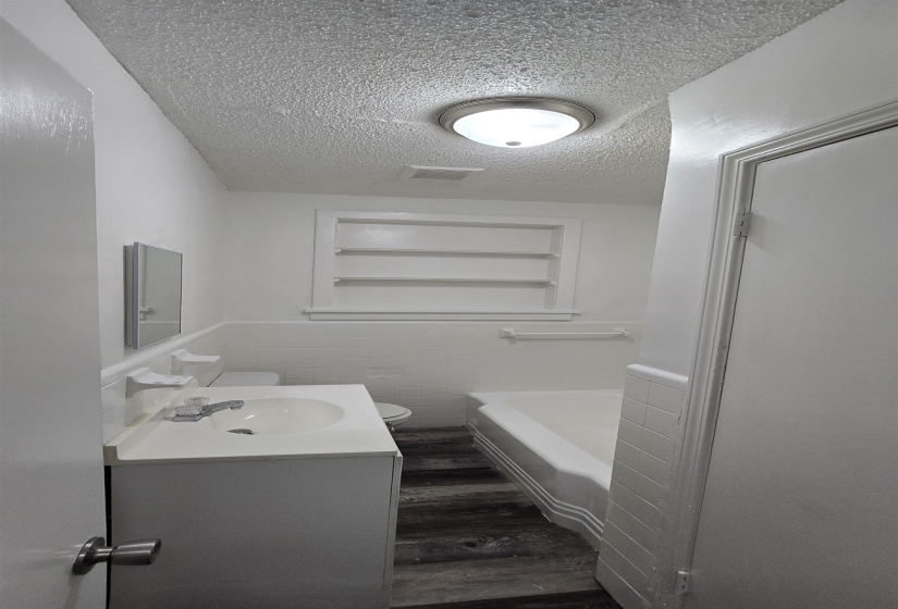 Bathroom with tile walls, a wainscoted wall, vanity, dark wood finished floors, and a textured ceiling