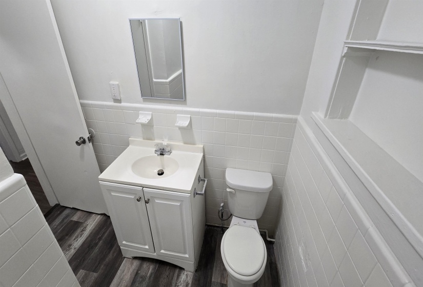 Half bath featuring tile walls, vanity, wainscoting, and dark wood-style floors