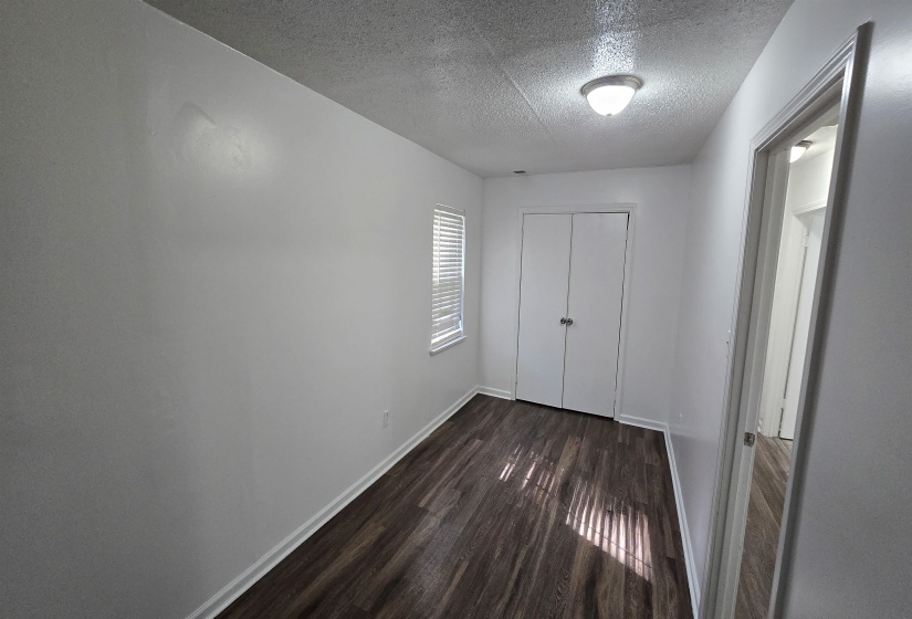 Unfurnished bedroom featuring a textured ceiling, dark wood finished floors, and a closet