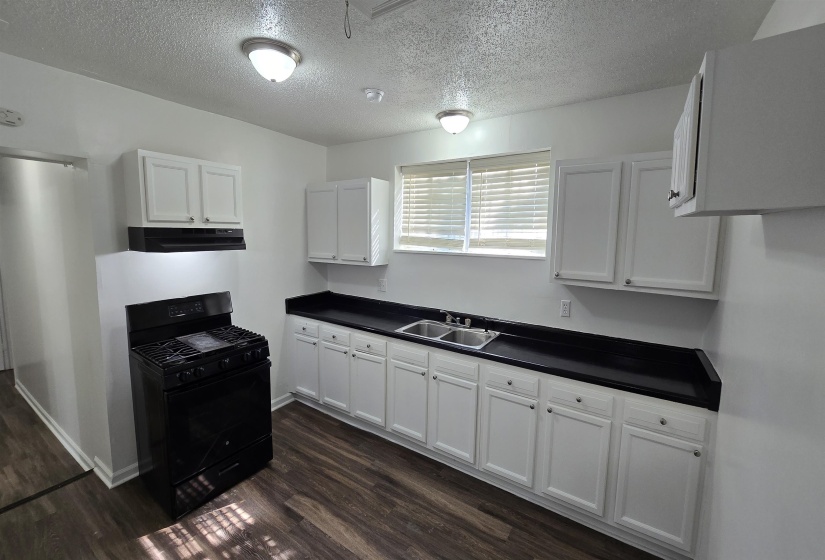 Kitchen with dark countertops, gas stove, white cabinetry, a textured ceiling, and dark wood finished floors
