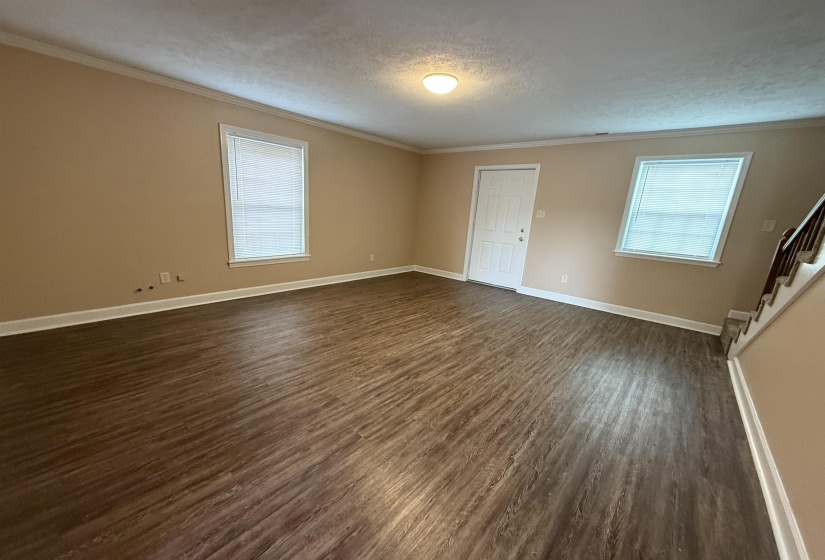 Unfurnished living room with crown molding, healthy amount of natural light, dark wood-style floors, a textured ceiling, and stairs