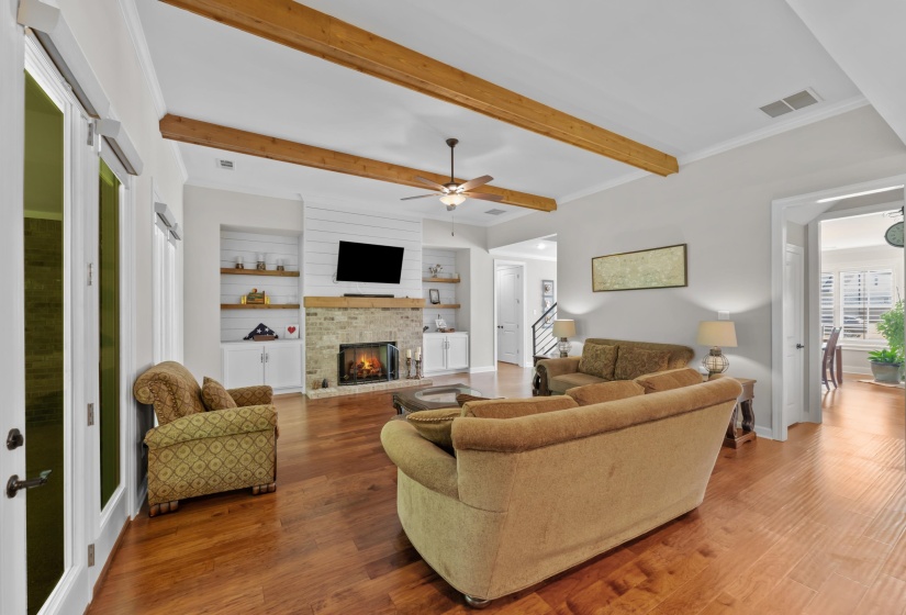 Living area with a brick fireplace, wood finished floors, a ceiling fan, beam ceiling, and stairway