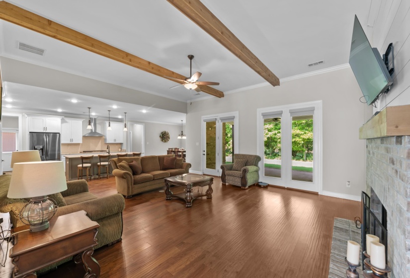 Living room with a ceiling fan, beamed ceiling, a fireplace, dark wood-style floors, and ornamental molding