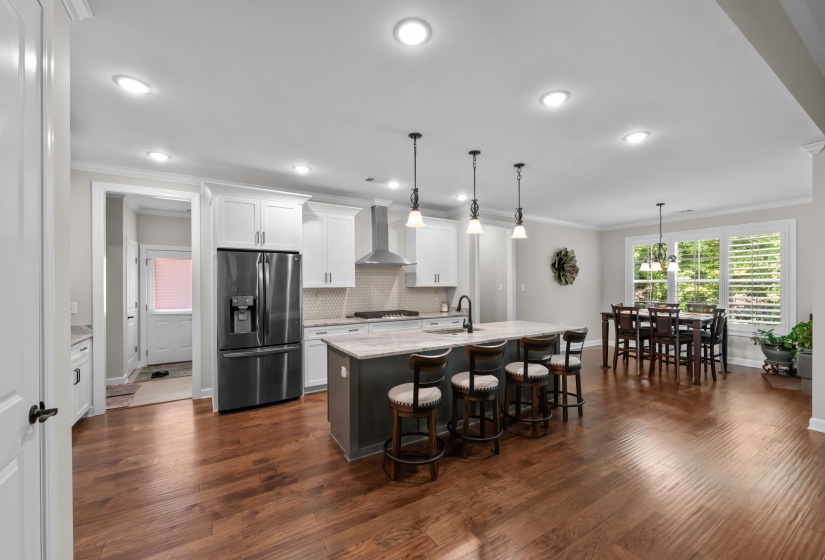 Kitchen with appliances with stainless steel finishes, wall chimney exhaust hood, a breakfast bar area, ornamental molding, and white cabinetry