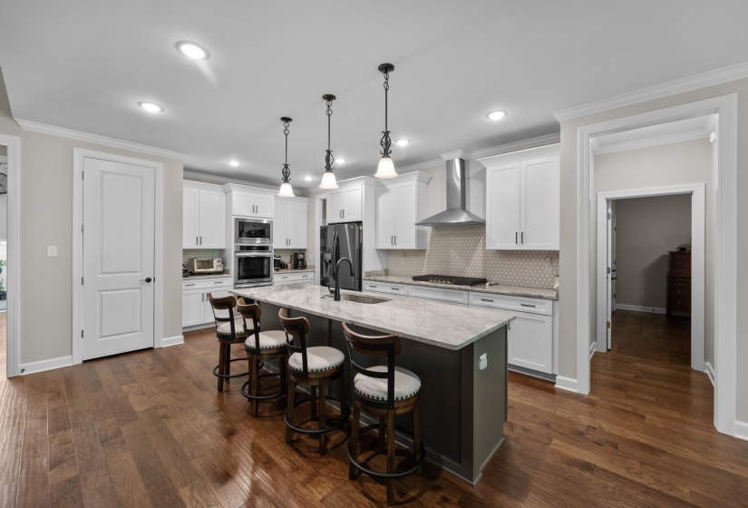 Kitchen with wall chimney range hood, appliances with stainless steel finishes, backsplash, a kitchen island with sink, and white cabinets