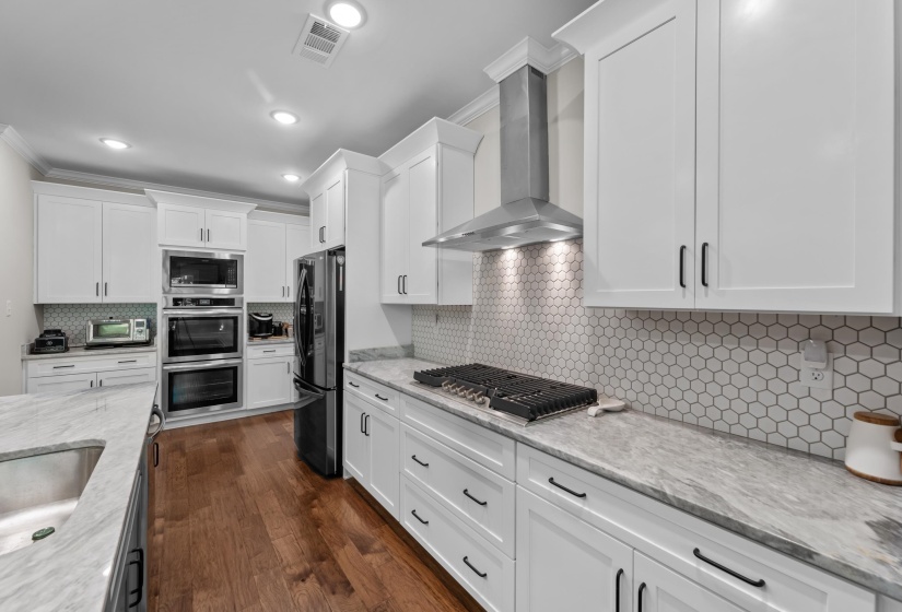 Kitchen with wall chimney exhaust hood, stainless steel appliances, tasteful backsplash, white cabinetry, and crown molding