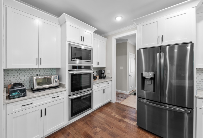 Kitchen with appliances with stainless steel finishes, ornamental molding, tasteful backsplash, white cabinets, and dark wood-type flooring