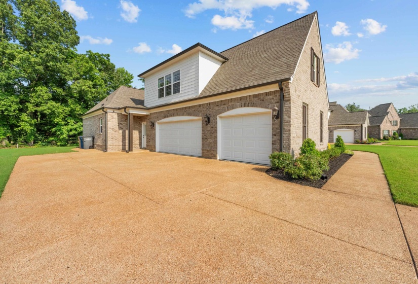 View of side of home featuring brick siding, concrete driveway, roof with shingles, and a yard
