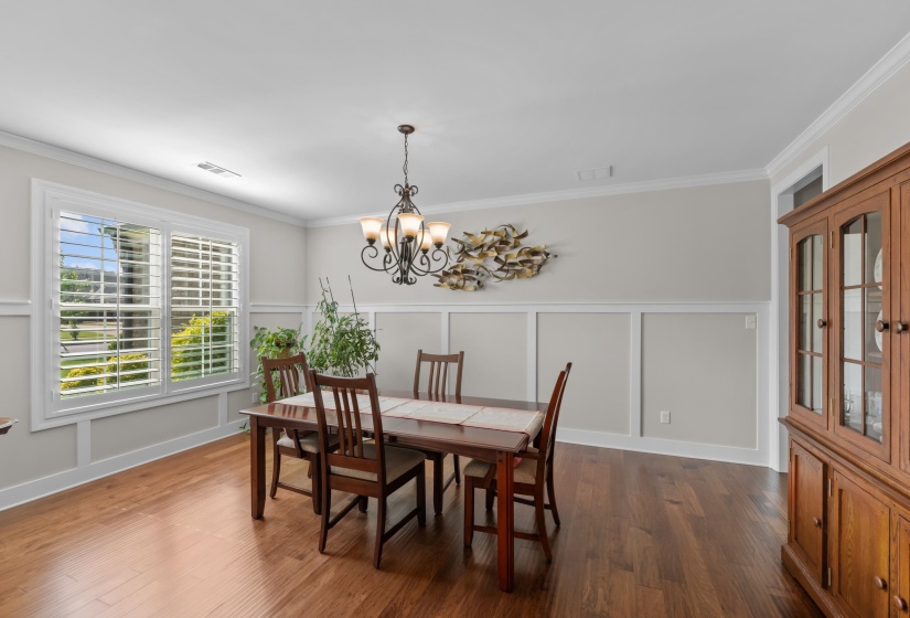 Dining room with a chandelier, crown molding, a decorative wall, dark wood finished floors, and a wainscoted wall