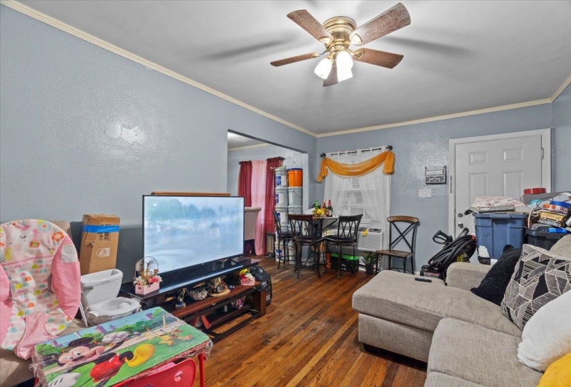 Living area with a textured wall, ornamental molding, dark wood finished floors, and a ceiling fan