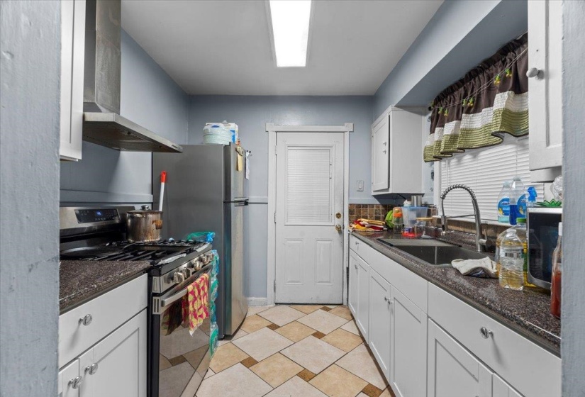 Kitchen with stainless steel appliances, wall chimney range hood, white cabinets, dark stone counters, and light tile patterned floors