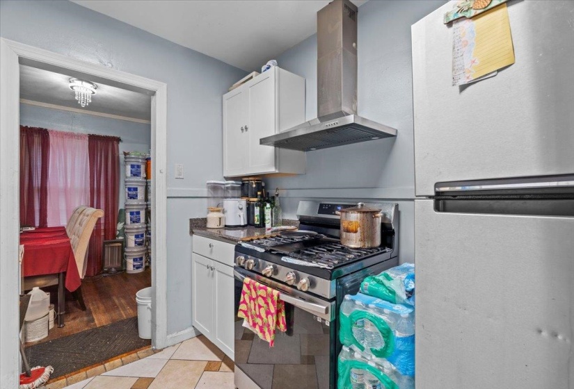 Kitchen with stainless steel appliances, exhaust hood, white cabinets, light tile patterned floors, and dark stone countertops