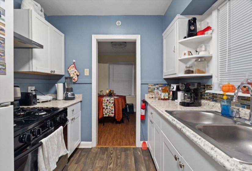 Kitchen with black gas range oven, white cabinetry, dark wood-type flooring, wall chimney range hood, and open shelves