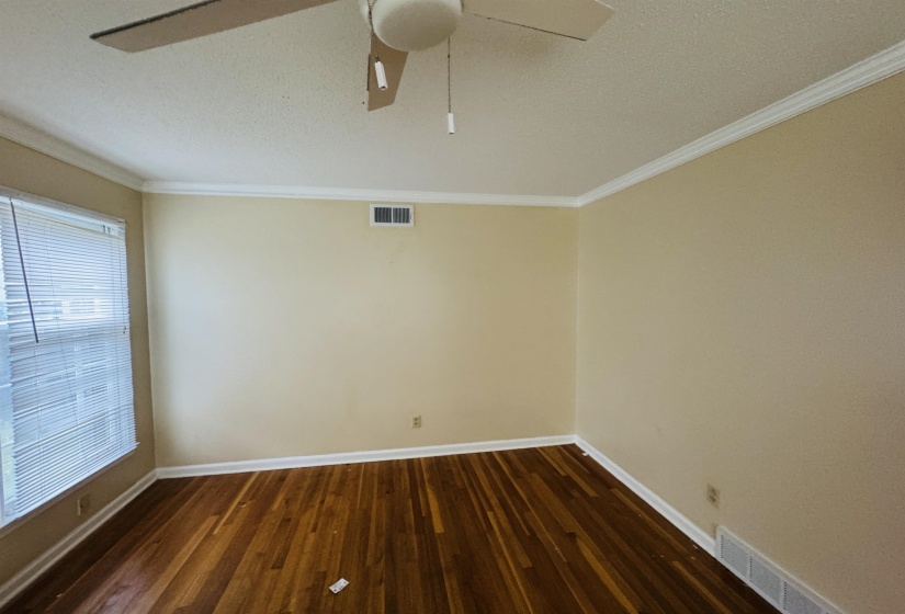Spare room featuring dark wood-style floors, baseboards, ornamental molding, and visible vents