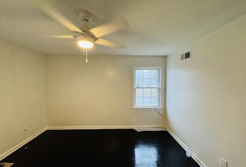 Unfurnished room featuring ceiling fan, a textured ceiling, visible vents, dark wood-style flooring, and baseboards