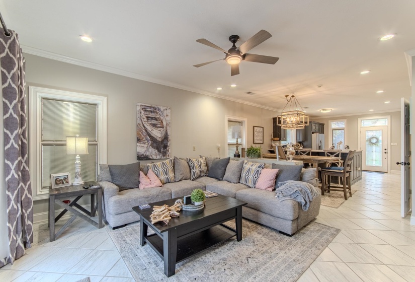 Living room with ornamental molding, light tile patterned flooring, ceiling fan, recessed lighting, and a chandelier