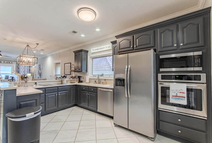 Kitchen featuring stainless steel appliances, ornamental molding, a chandelier, a peninsula, and hanging light fixtures