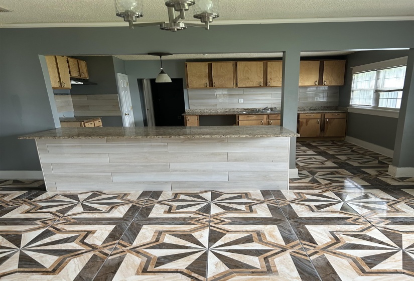 Kitchen featuring a textured ceiling, baseboards, decorative backsplash, brown cabinetry, and decorative light fixtures