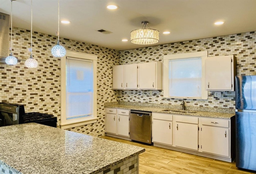 Kitchen with freestanding refrigerator, light stone countertops, recessed lighting, stainless steel dishwasher, and backsplash