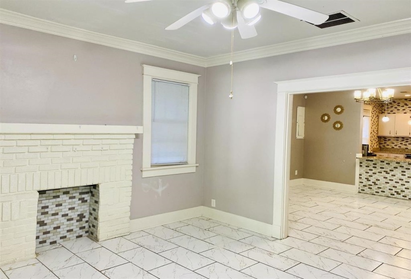 Unfurnished living room featuring ornamental molding, a chandelier, light marble finish flooring, and a brick fireplace
