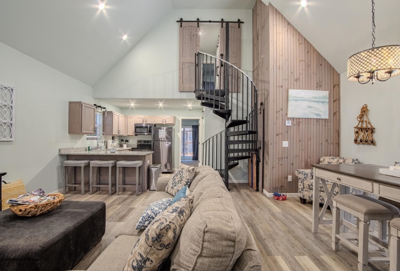 Living area with a barn door, high vaulted ceiling, stairs, light wood finished floors, and wooden walls