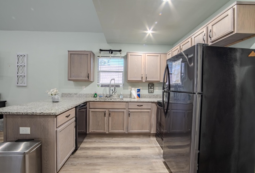Kitchen with black appliances, a peninsula, light stone countertops, and light wood-type flooring