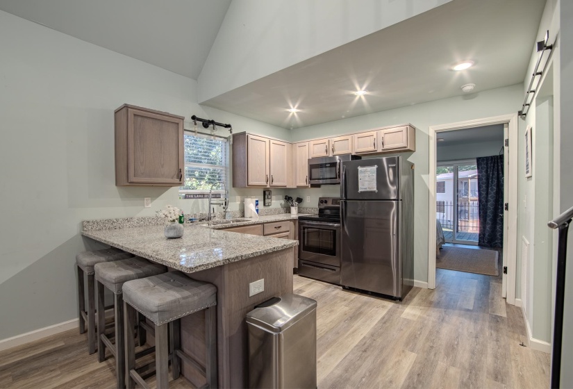 Kitchen with appliances with stainless steel finishes, light stone countertops, a peninsula, a kitchen breakfast bar, and light wood finished floors