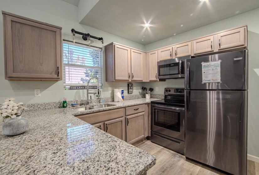 Kitchen with stainless steel appliances, light stone counters, light wood-style floors, and light brown cabinets