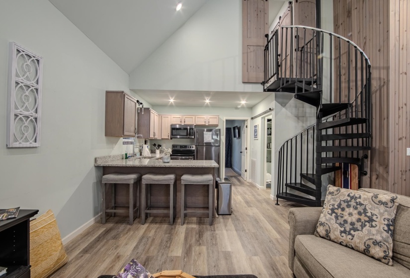 Kitchen featuring high vaulted ceiling, a kitchen breakfast bar, light stone counters, appliances with stainless steel finishes, and light wood-style floors