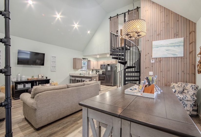 Living area featuring stairway, high vaulted ceiling, wood walls, light wood-style floors, and a barn door