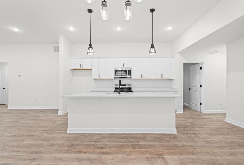 Kitchen featuring white cabinetry, decorative light fixtures, stainless steel appliances, an island with sink, and light wood-style flooring