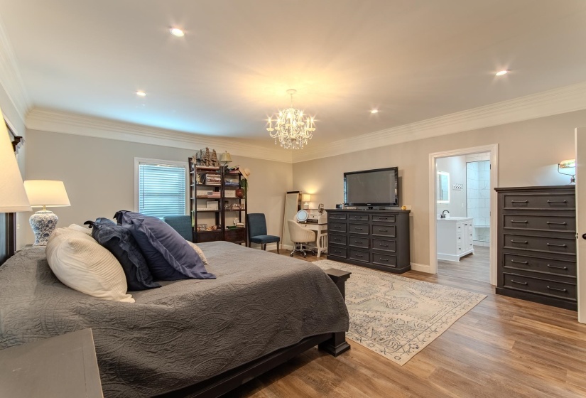 Bedroom with wood finished floors, a chandelier, crown molding, recessed lighting, and connected bathroom
