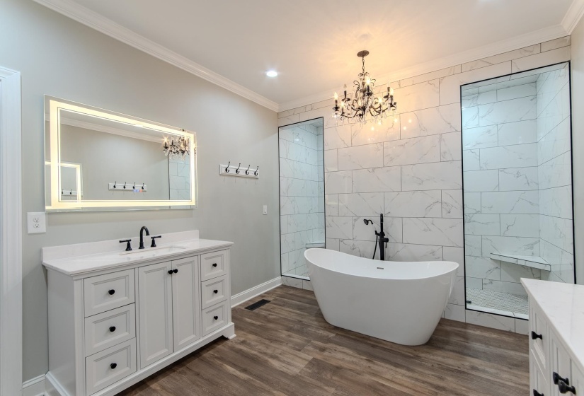 Full bathroom with vanity, crown molding, a walk in shower, a freestanding bath, and dark wood-type flooring