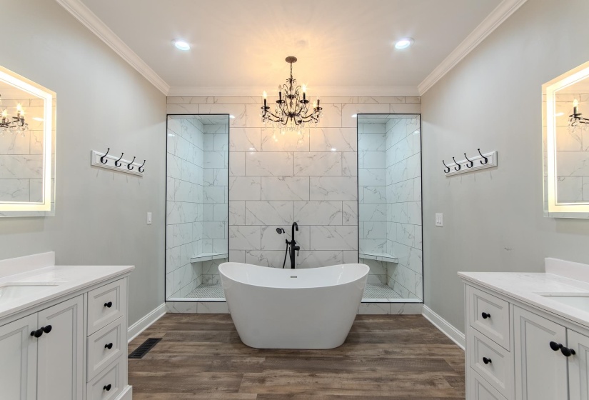 Bathroom with a chandelier, two vanities, dark wood-style flooring, a freestanding tub, and ornamental molding