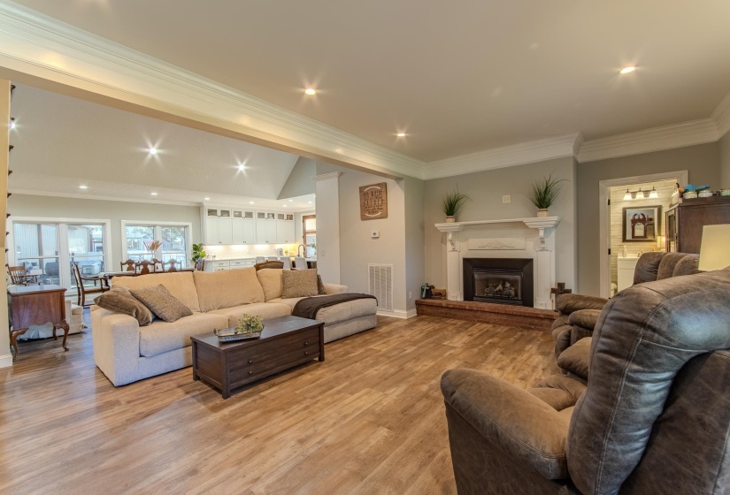 Living room with recessed lighting, ornamental molding, a fireplace with raised hearth, vaulted ceiling, and light wood-type flooring