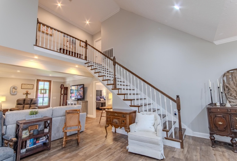 Living room with crown molding, a high ceiling, wood finished floors, recessed lighting, and stairway
