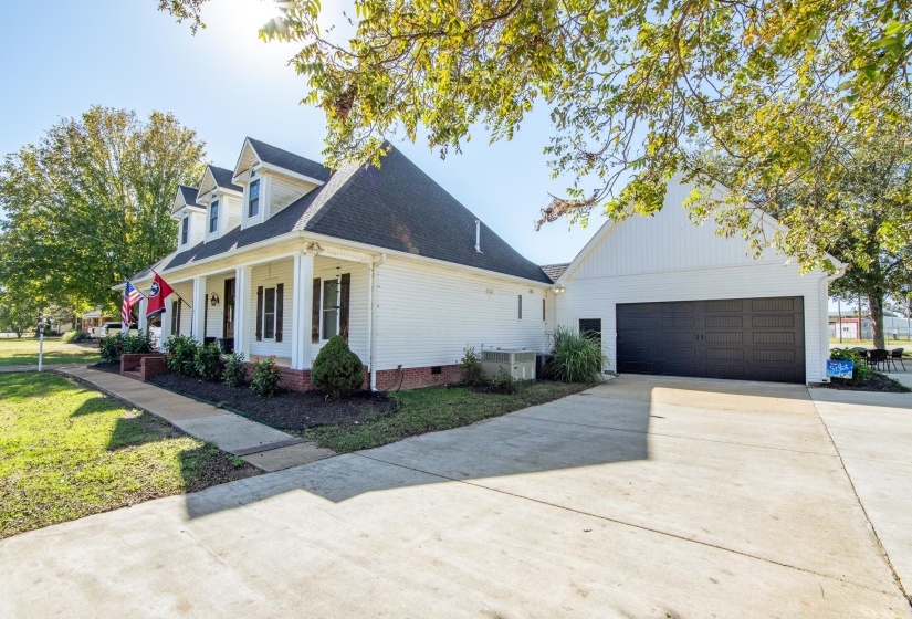 View of front of property featuring a porch, a garage, concrete driveway, a shingled roof, and a front yard