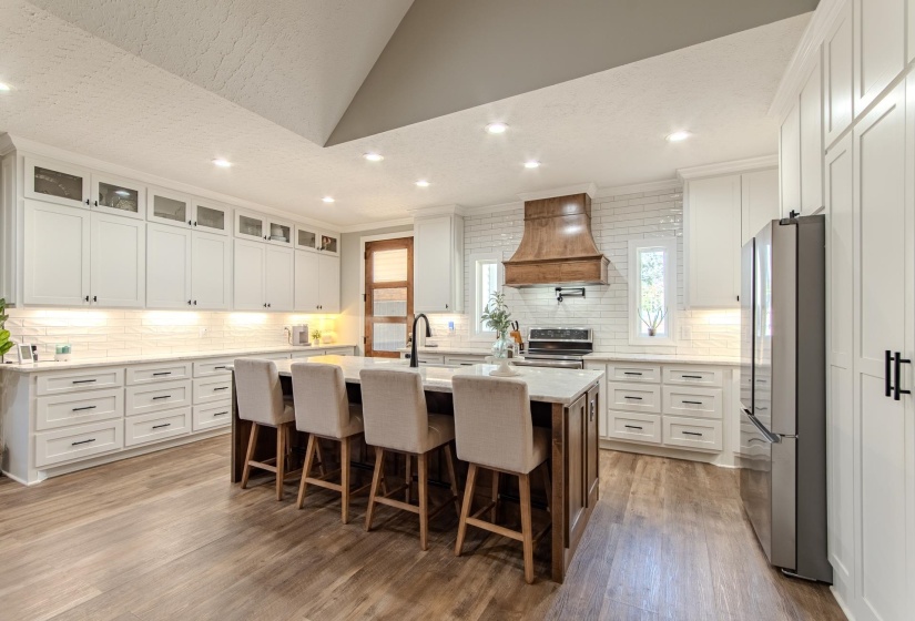 Kitchen featuring white cabinetry, a center island with sink, a kitchen bar, light stone counters, and recessed lighting