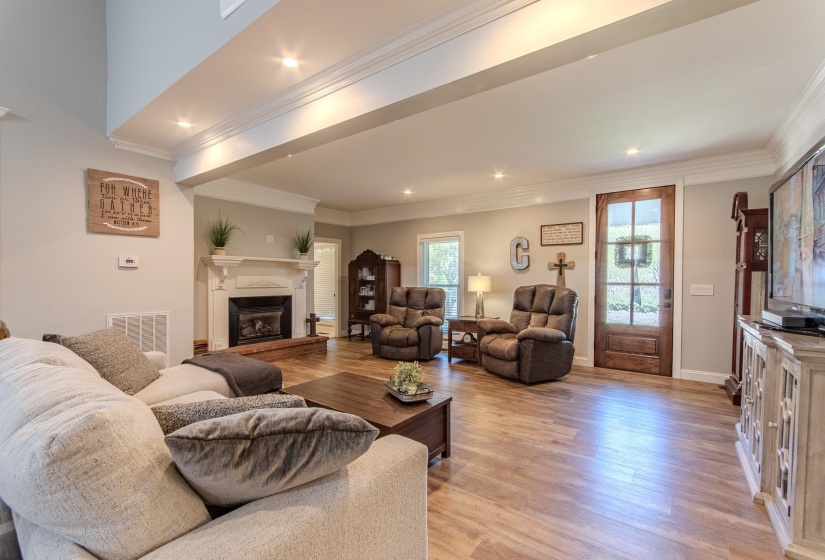 Living room with light wood-style floors, ornamental molding, a fireplace with raised hearth, and recessed lighting