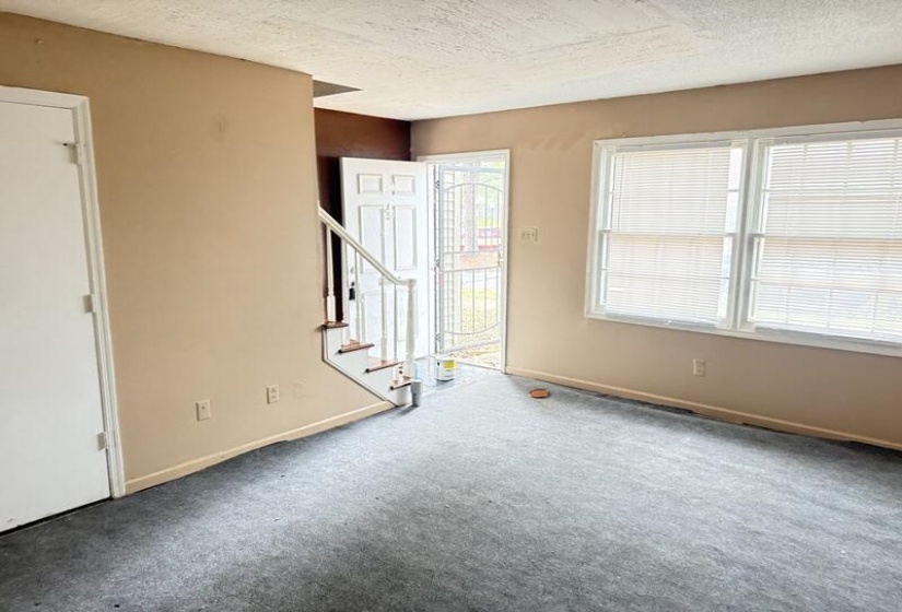 Unfurnished living room with a textured ceiling, stairway, and carpet