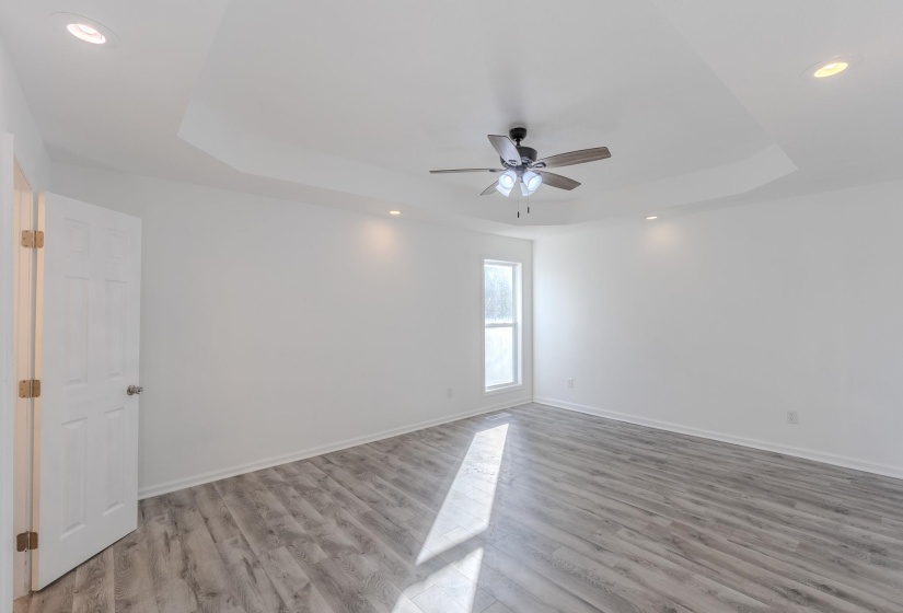 Empty room with a raised ceiling, recessed lighting, light wood-type flooring, and ceiling fan