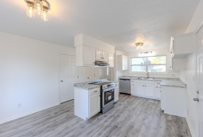 Kitchen with stainless steel appliances, white cabinetry, light wood finished floors, and light stone countertops