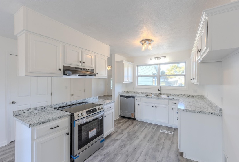 Kitchen featuring stainless steel appliances, white cabinetry, light wood-type flooring, under cabinet range hood, and light stone countertops