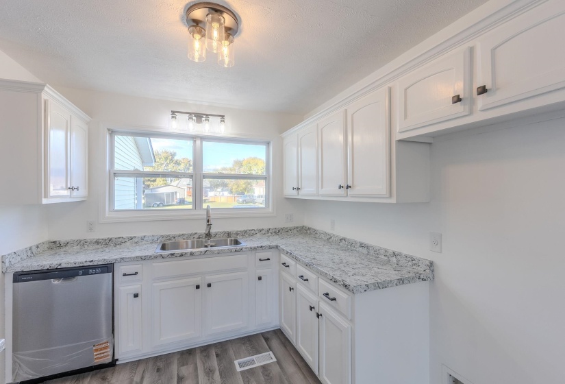 Kitchen with stainless steel dishwasher, white cabinets, and light wood-type flooring