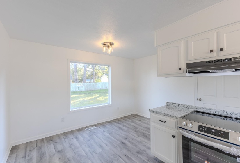 Kitchen featuring stainless steel range with electric cooktop, white cabinets, under cabinet range hood, light wood-style floors, and light stone countertops