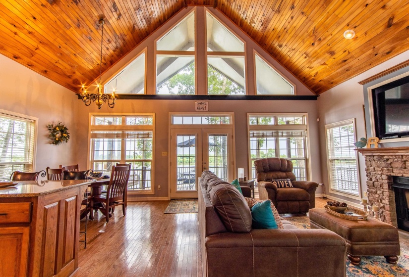Living room featuring high vaulted ceiling, wood-type flooring, french doors, a fireplace, and a chandelier