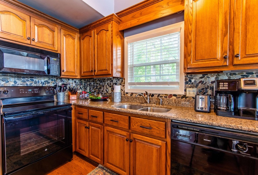 Kitchen with black appliances, light stone countertops, decorative backsplash, and brown cabinets