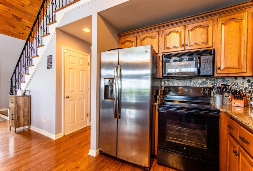 Kitchen with black appliances, brown cabinets, light stone countertops, light wood-type flooring, and tasteful backsplash